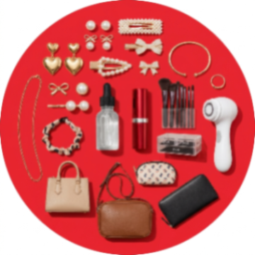 A curated flat-lay of assorted beauty, fashion, and accessories arranged in a circular pattern on a solid red background. The collection includes gold and pearl jewelry, hair accessories, makeup brushes, a white handheld device, a small handbag, a brown leather pouch, a black wallet, and a clear bottle with a black dropper cap.